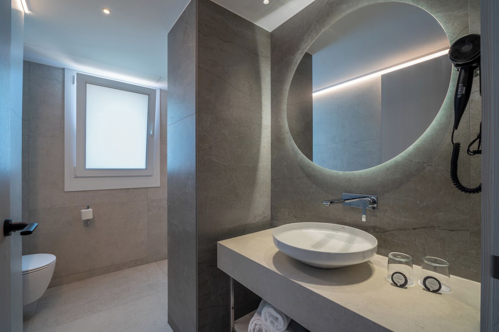 A modern bathroom with a round mirror, a sink, and a hairdryer.