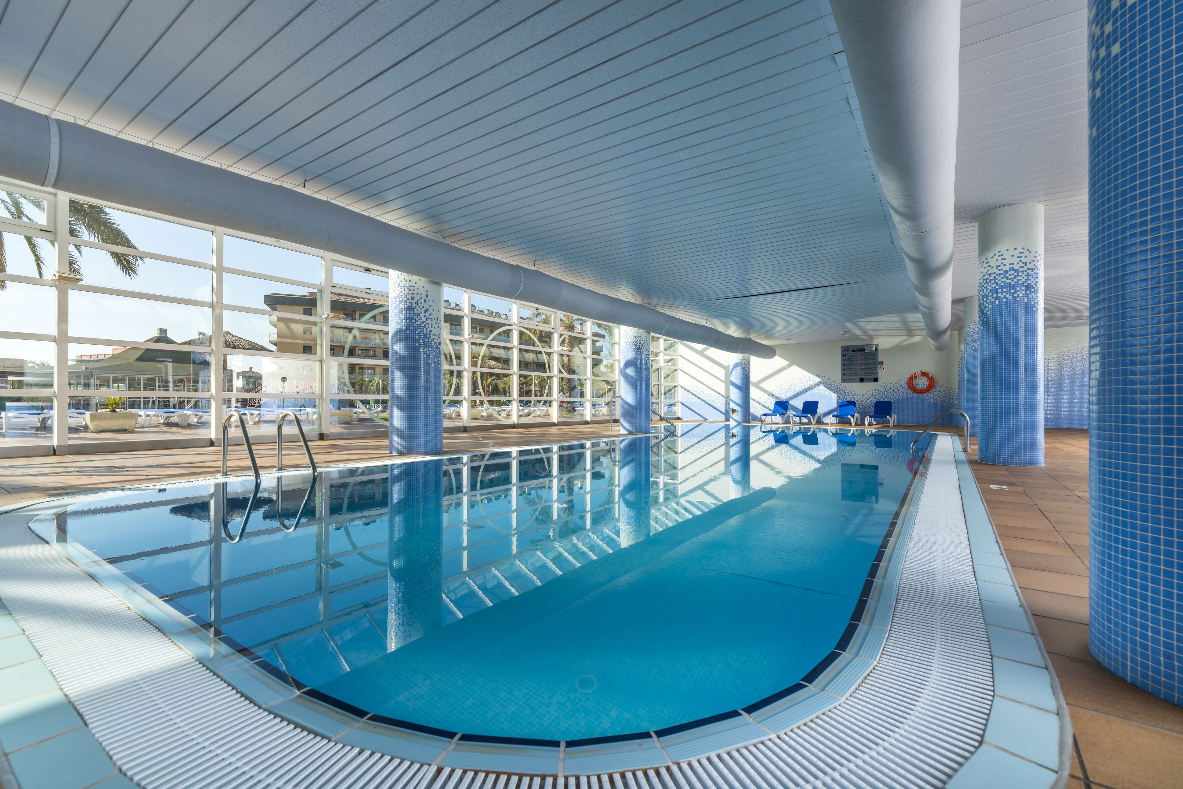 Una piscina interior con agua azul cristalina, tragaluces y vistas al exterior.