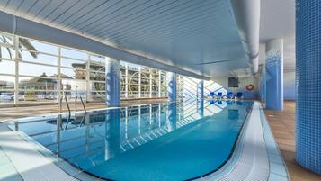 Una piscina interior con agua azul cristalina, tragaluces y vistas al exterior.