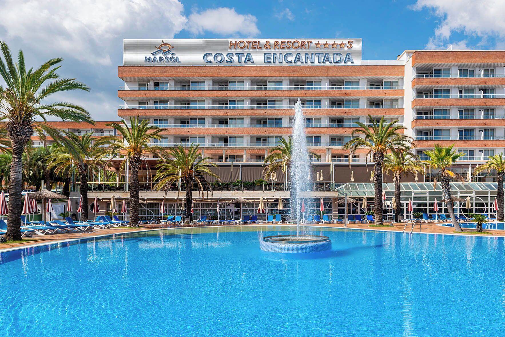 A hotel with a large pool, palm trees, and a fountain.