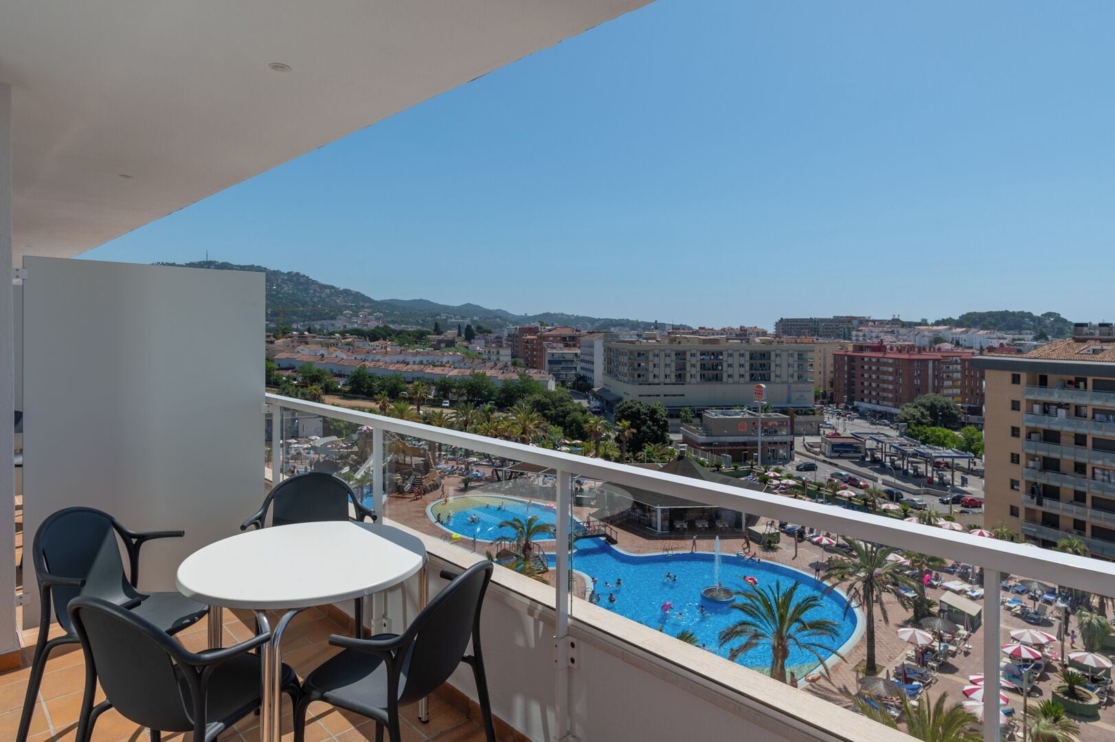 Un balcón con mesa y sillas, con vistas a una piscina y al paisaje urbano.