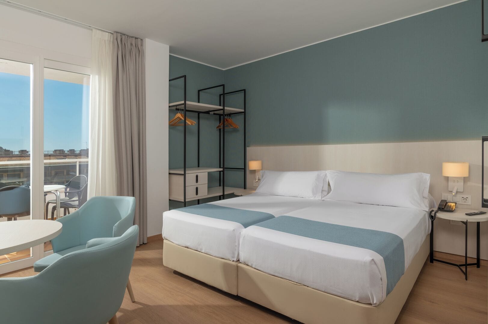 A hotel room with a bed, two bedside tables, a chair, a desk, and a wardrobe.
