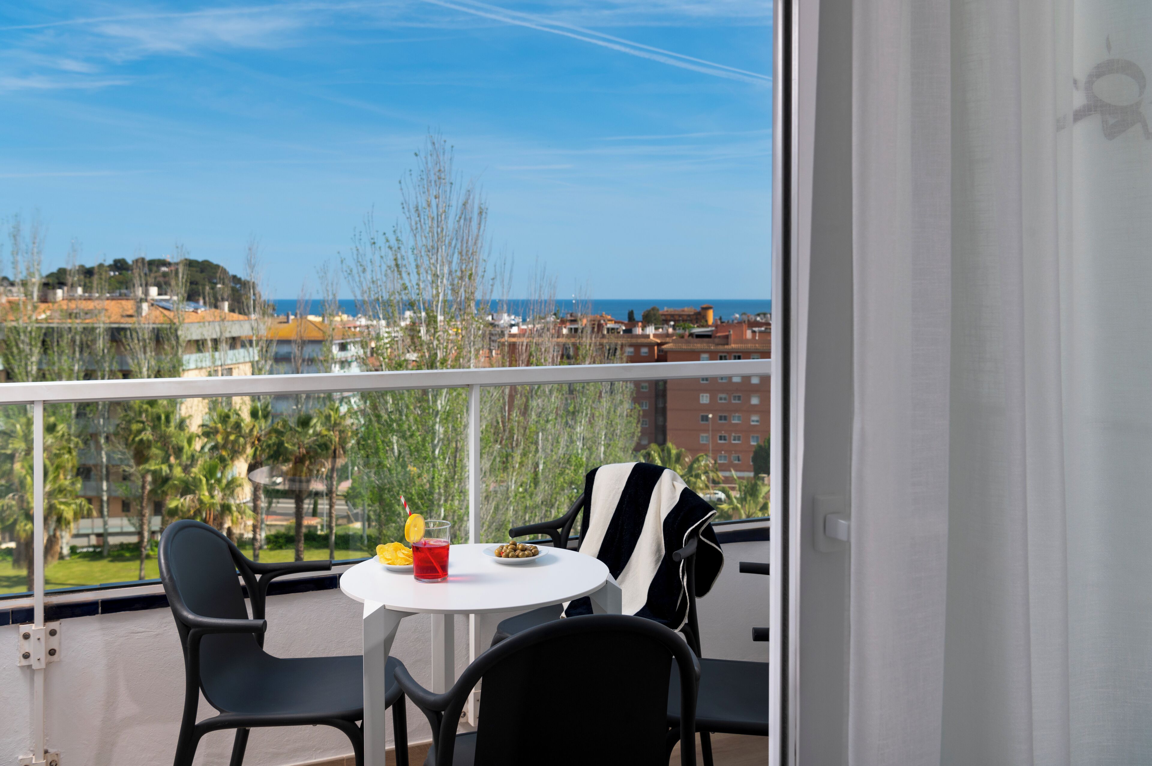 Un balcon avec une table, des chaises et une vue sur la mer et les bâtiments.