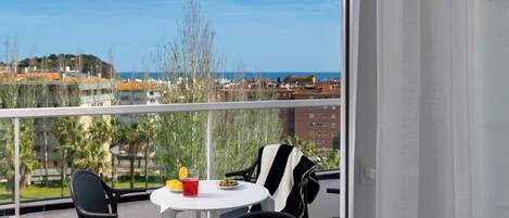 A balcony with a table, chairs, and a view of the sea and buildings.