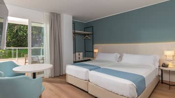 Habitación de hotel con una cama grande, una mesita pequeña, una silla, un balcón con vistas a zonas verdes y un armario.