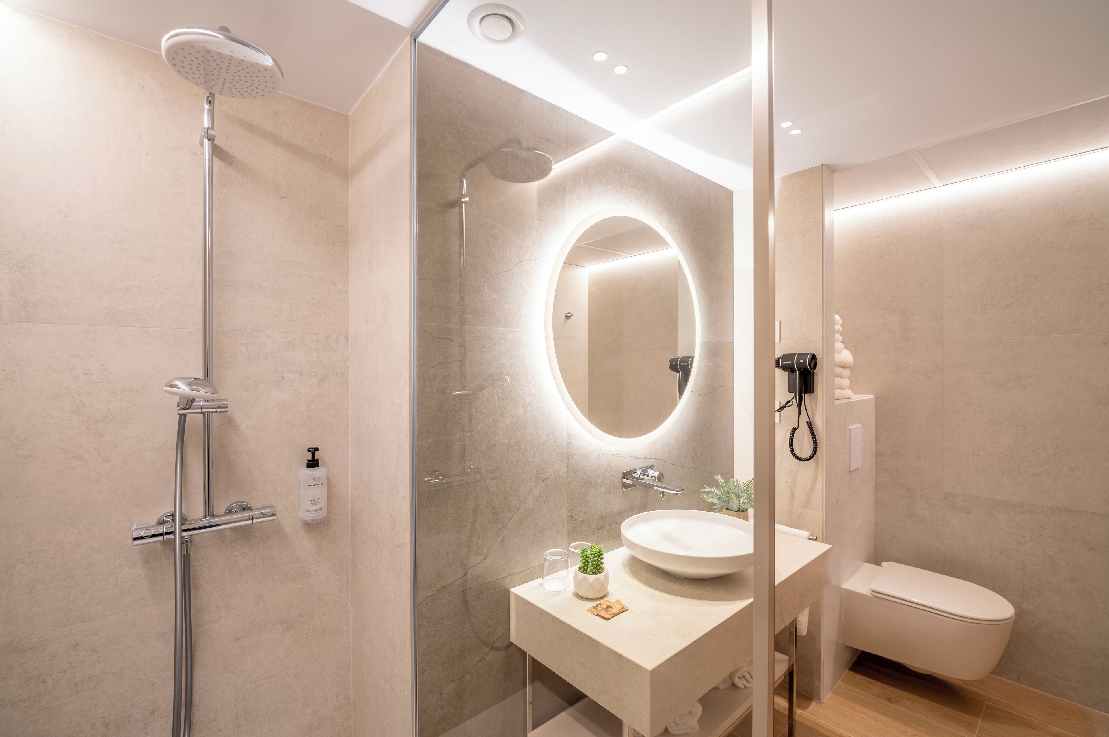 Un baño moderno con ducha de vidrio, un espejo redondo, un lavabo y un inodoro.