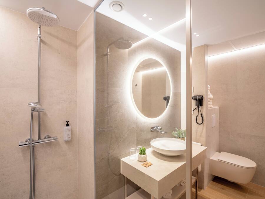 Un baño moderno con ducha de vidrio, un espejo redondo, un lavabo y un inodoro.