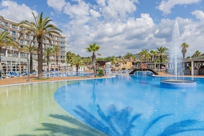 Une grande piscine avec une fontaine, entourée de palmiers et d’un bâtiment d’hôtel doté de balcons.