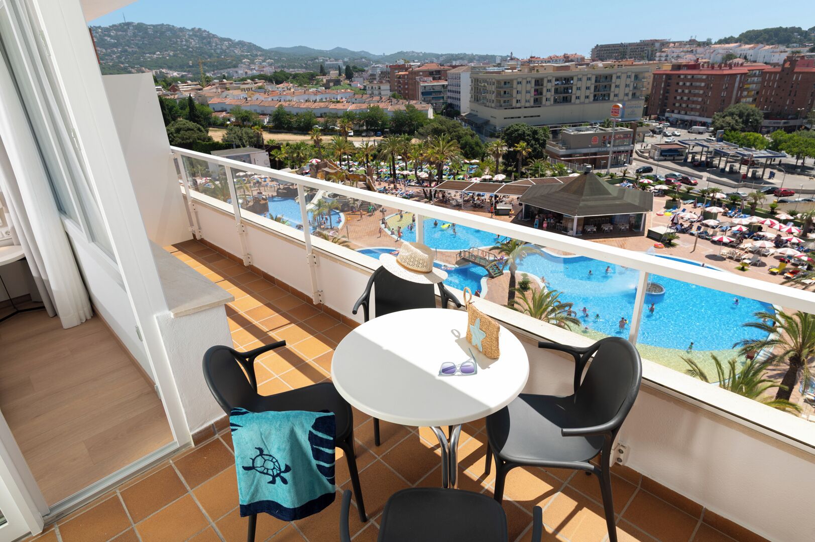 Un balcón con vistas a una piscina, sillas, una mesa y una sombrilla.
