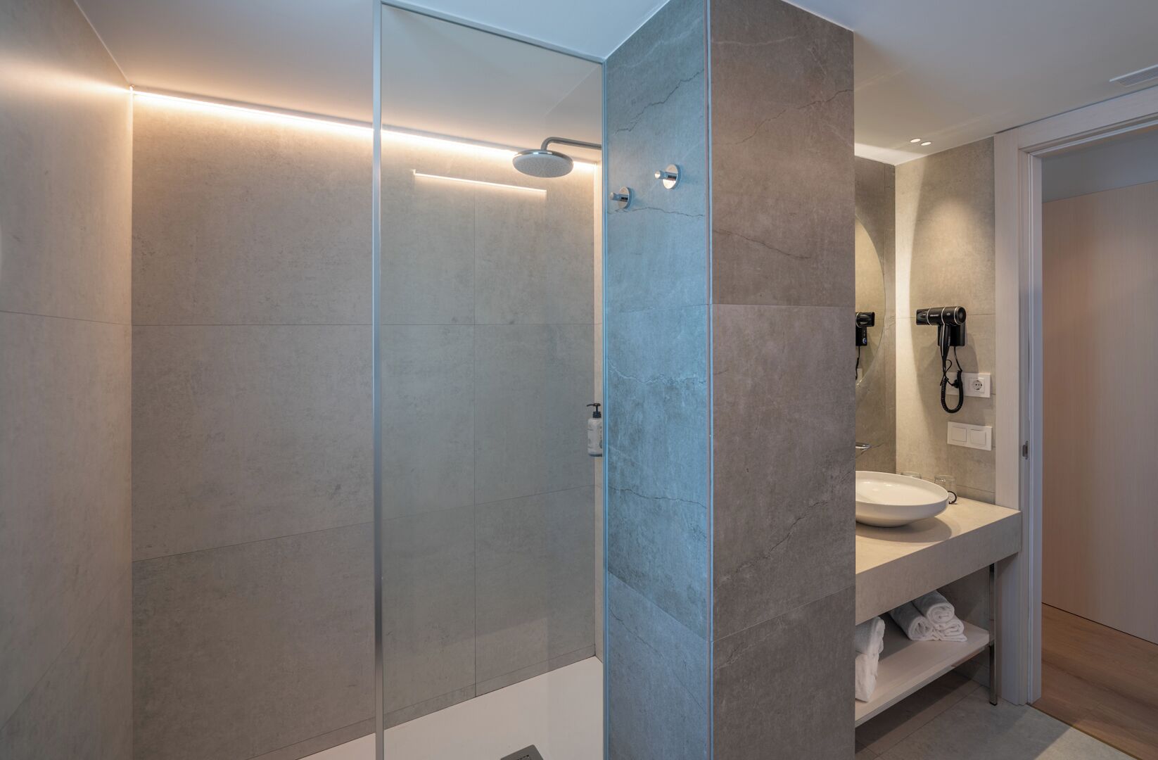 A modern bathroom with a glass-enclosed shower, a sink with a towel rack, and a hairdryer mounted on the wall.