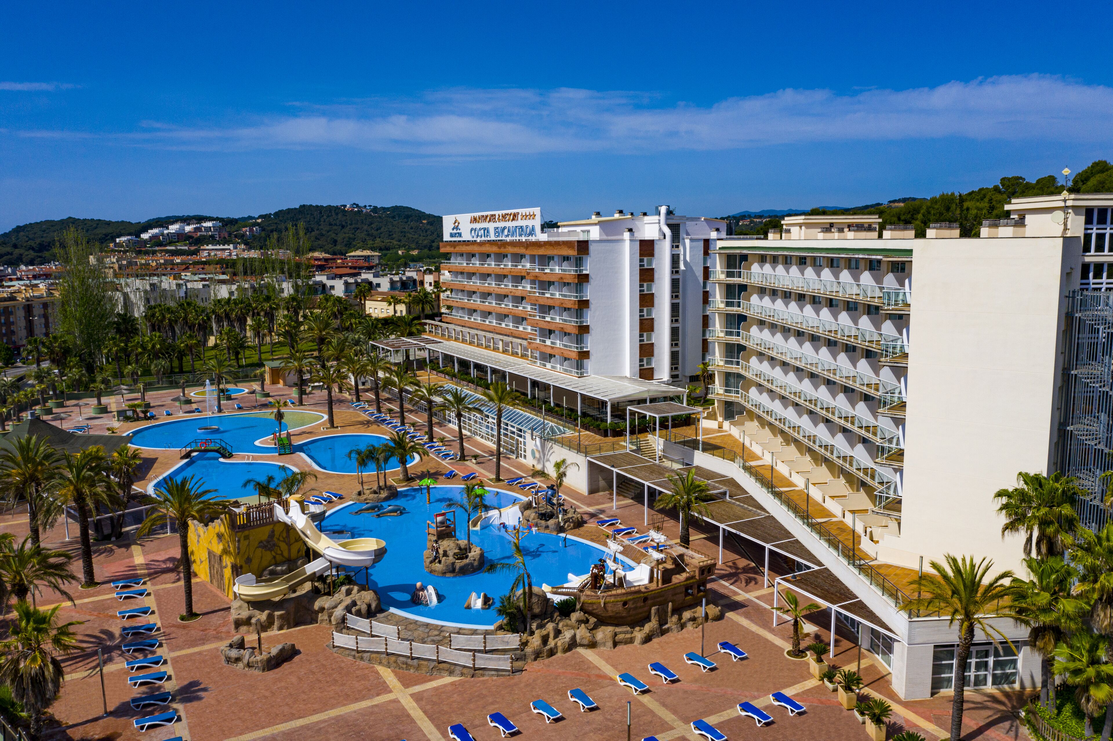 Un hotel con múltiples piscinas, un edificio grande con balcones y una zona ajardinada circundante con palmeras.