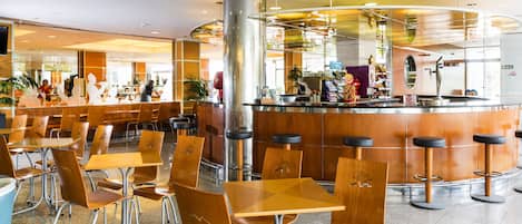 Un restaurante moderno con mesas y sillas de madera, una barra central y un panel de vidrio que separa el comedor de la barra.