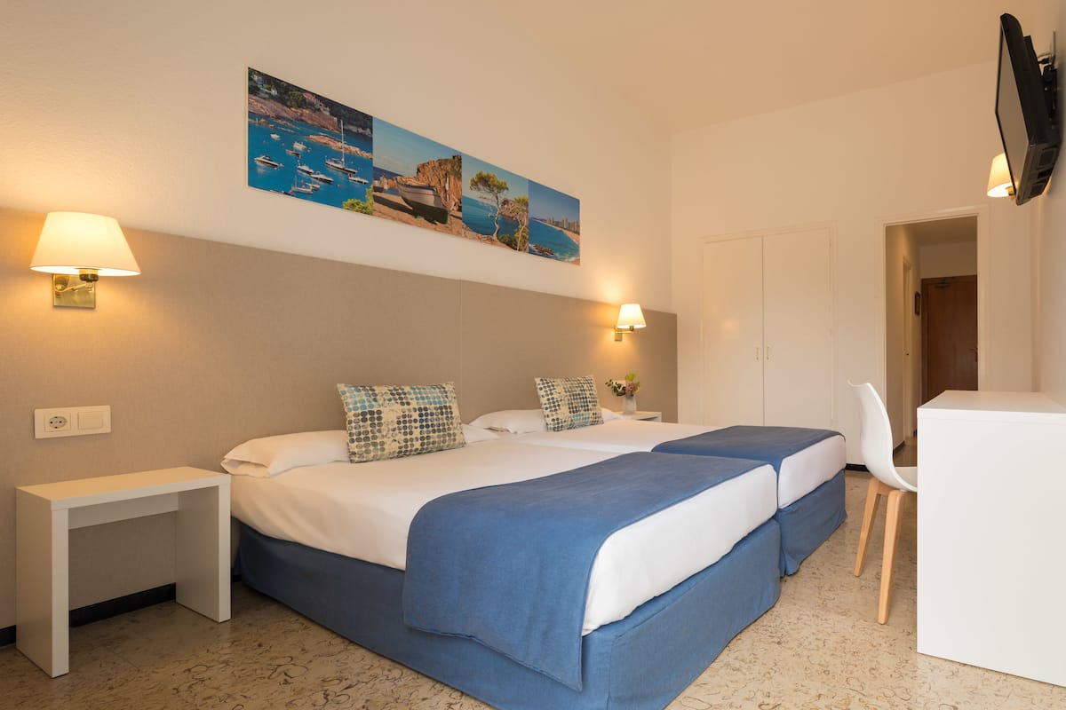 A hotel room with two beds, a desk, a chair, and a TV mounted on the wall.