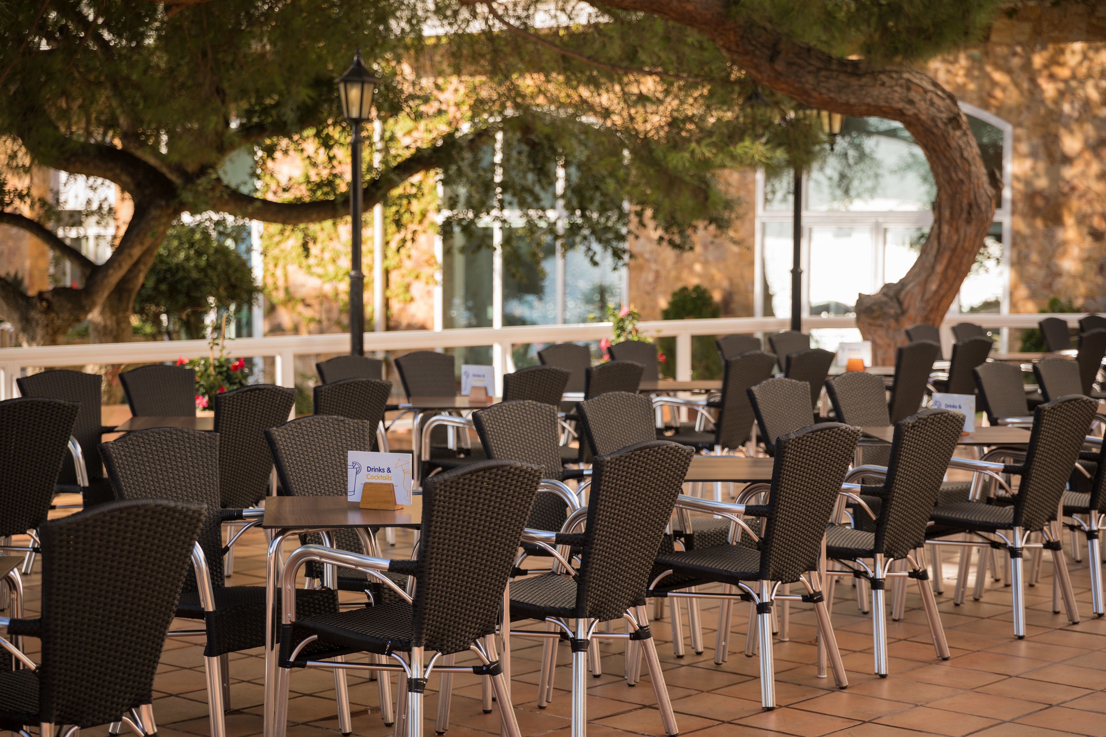 Un restaurant doté d’une terrasse, de chaises en osier et d ’un panneau indiquant les plats proposés au menu.