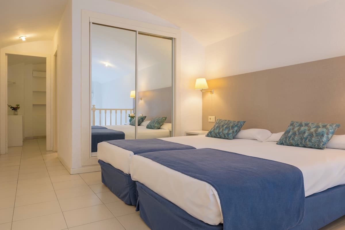 A hotel room with two beds, a sliding door closet, a bedside lamp, and a view of the hallway.