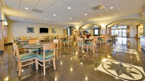 Un hall d’hôtel spacieux, doté de nombreuses tables et chaises, d’un comptoir d’accueil et d’une grande fenêtre laissant entrer la lumière naturelle.