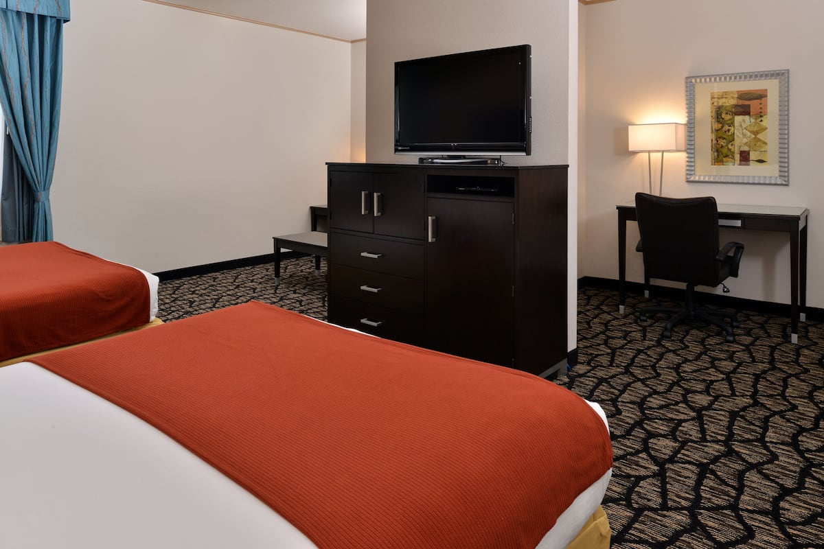 Une chambre d’hôtel avec deux lits, un téléviseur posé sur un meuble, un bureau avec une chaise et une moquette à motifs.