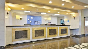 A hotel reception desk with a blue sign, multiple light fixtures, and a polished floor.