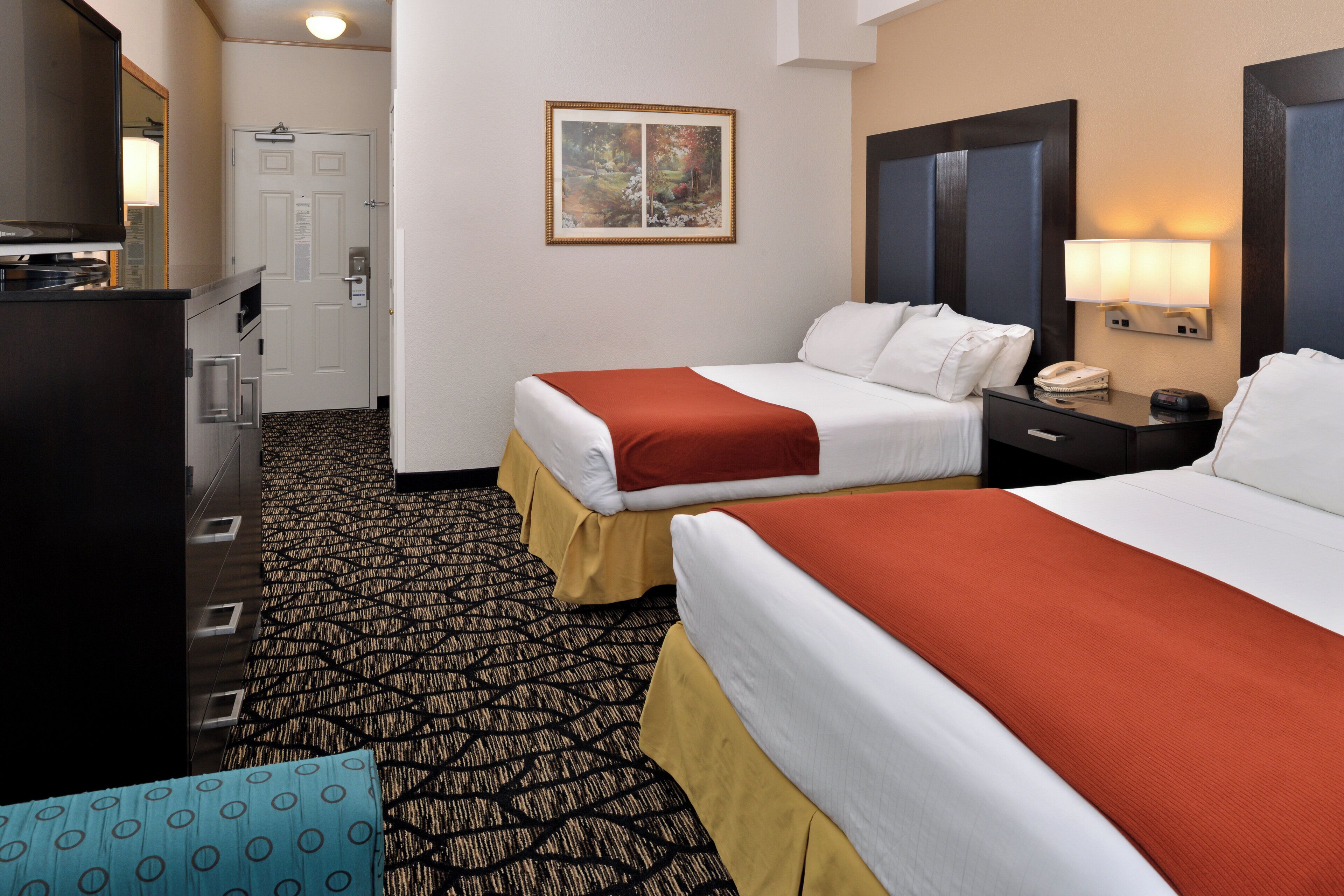 A hotel room with two beds, a desk, a chair, a dresser, and a painting on the wall.