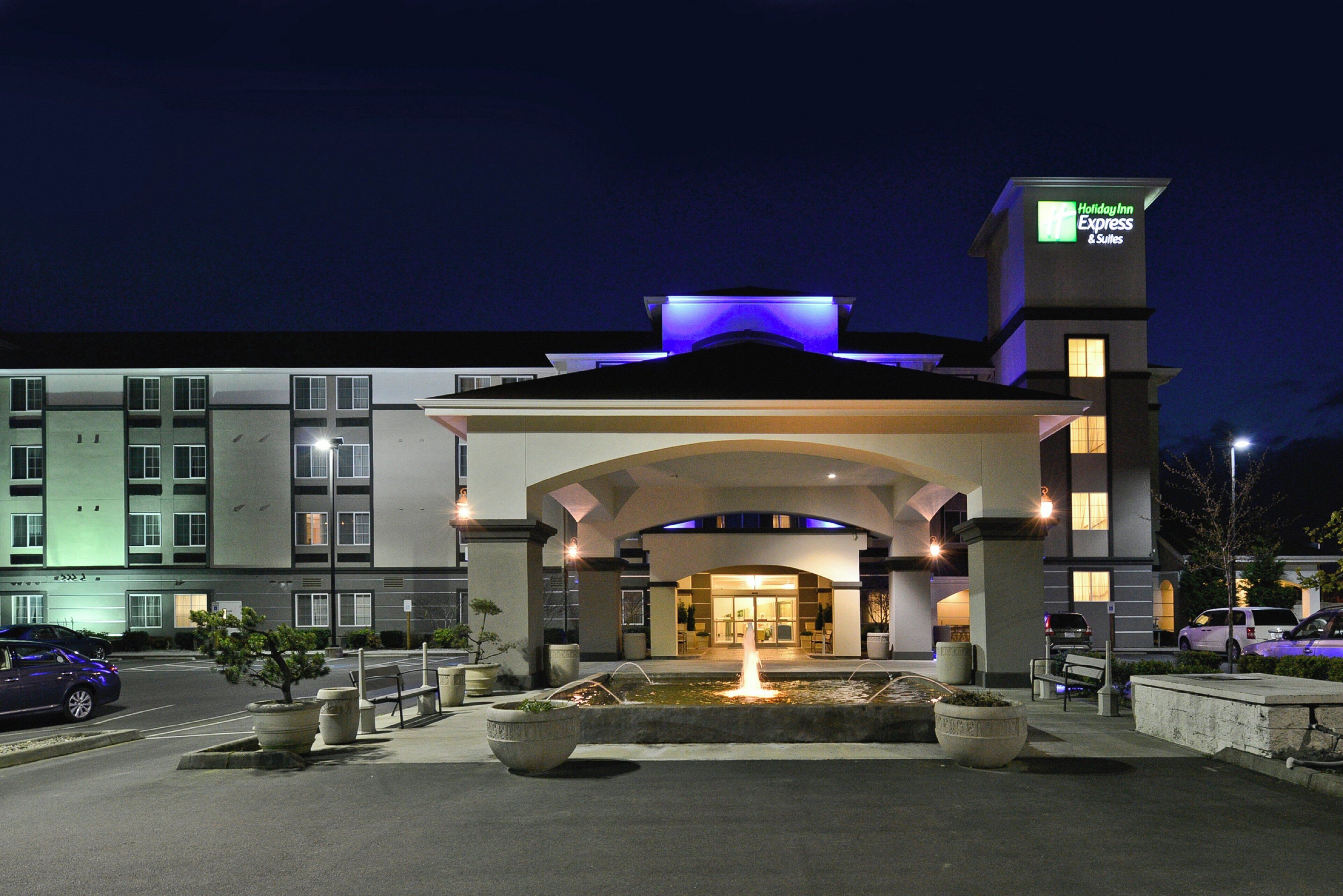 L’entrée d’un hôtel avec une fontaine, une enseigne indiquant « Holiday Inn Express & Suites » et un parking.