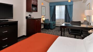 A hotel room with a bed, a desk with a chair, a television, a microwave, and a coffee maker.