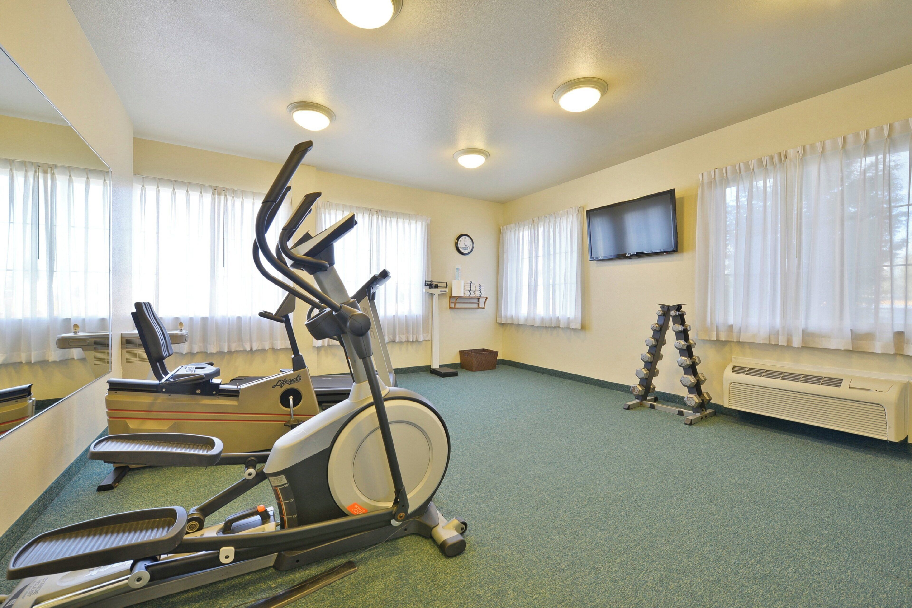 A gym with exercise equipment, a television, and a clock on the wall.