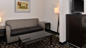 A hotel room with a sofa, a coffee table, a flat-screen TV on a cabinet, a framed artwork on the wall, and a lamp. - Holiday Inn Express & Suites Tacoma South - Lakewood by IHG (Lakewood)