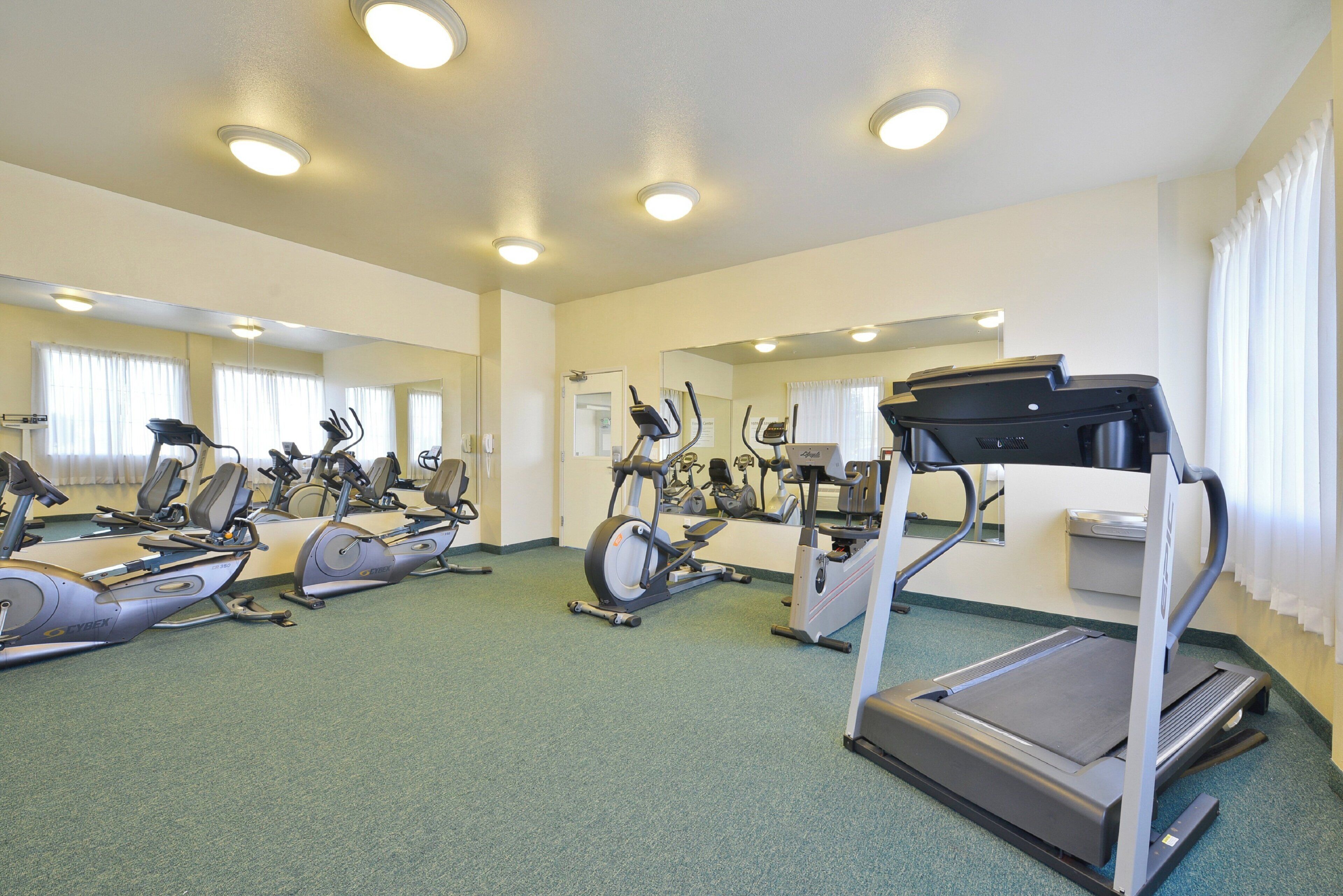 A gym with multiple exercise machines, including treadmills and stationary bikes, and mirrors on the walls.