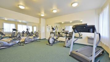 A gym with multiple exercise machines, including treadmills and stationary bikes, and mirrors on the walls.