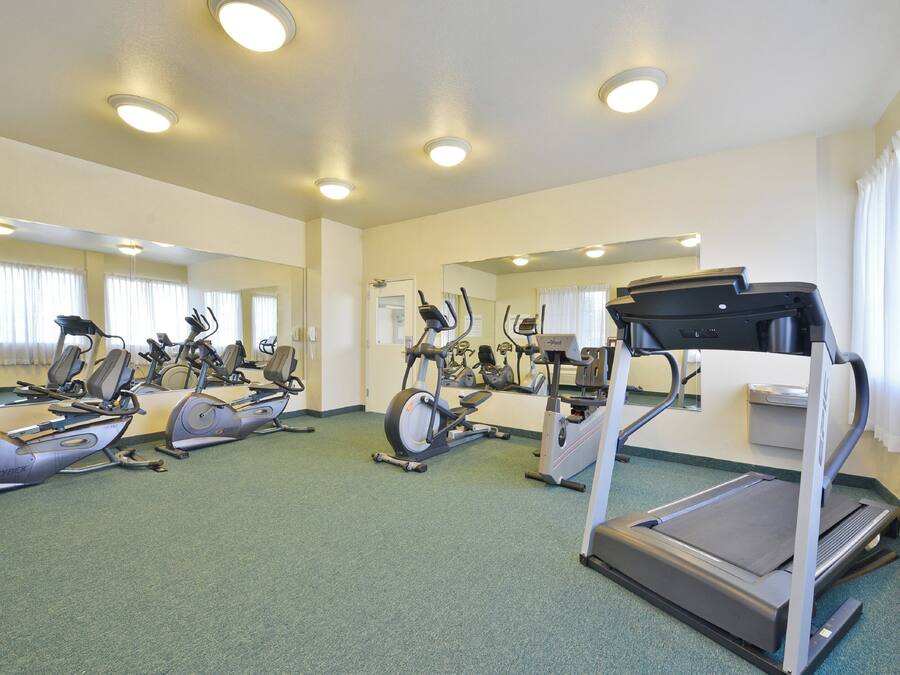 A gym with multiple exercise machines, including treadmills and stationary bikes, and mirrors on the walls.