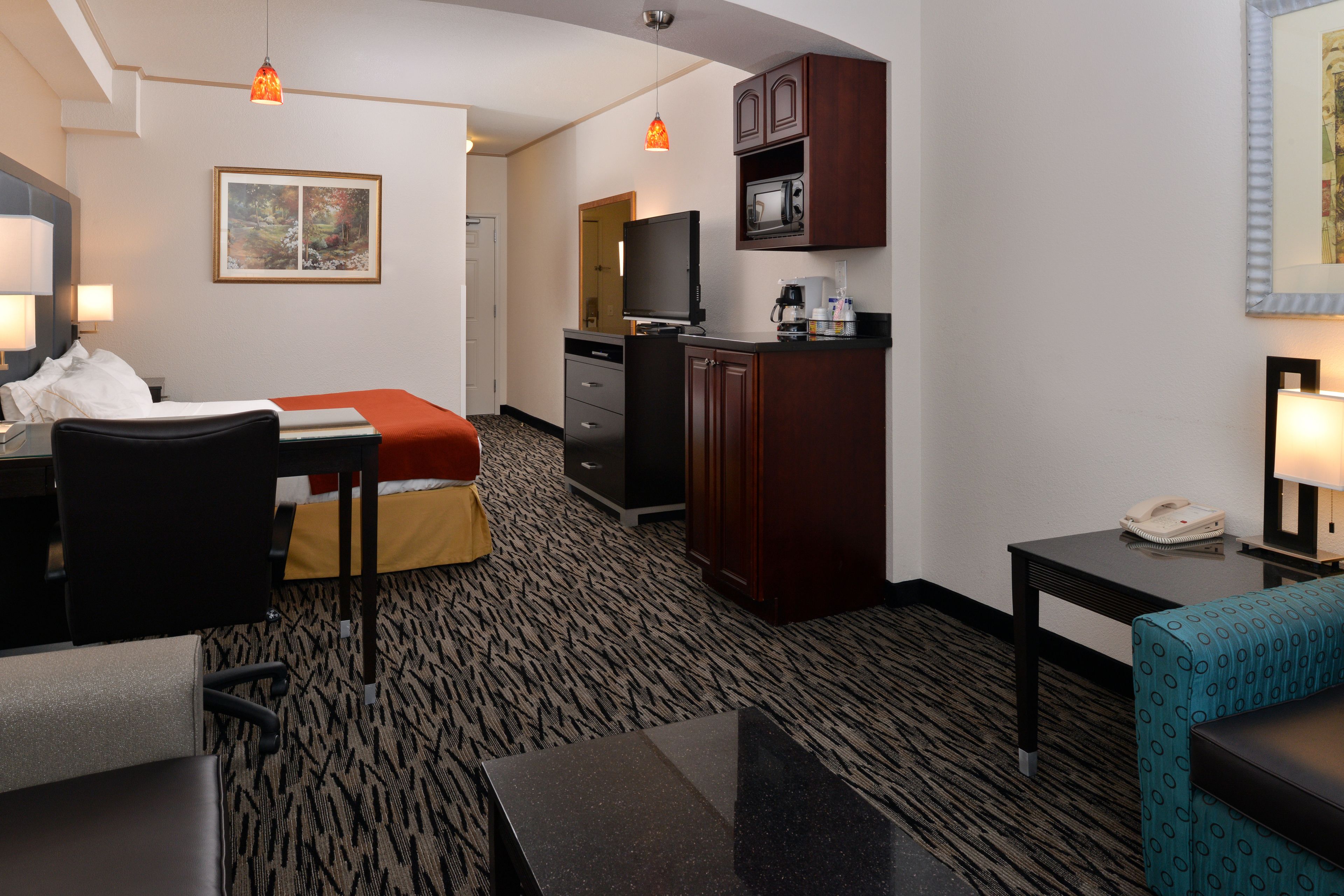 A hotel room with a bed, desk, chair, kitchenette, and a small seating area.