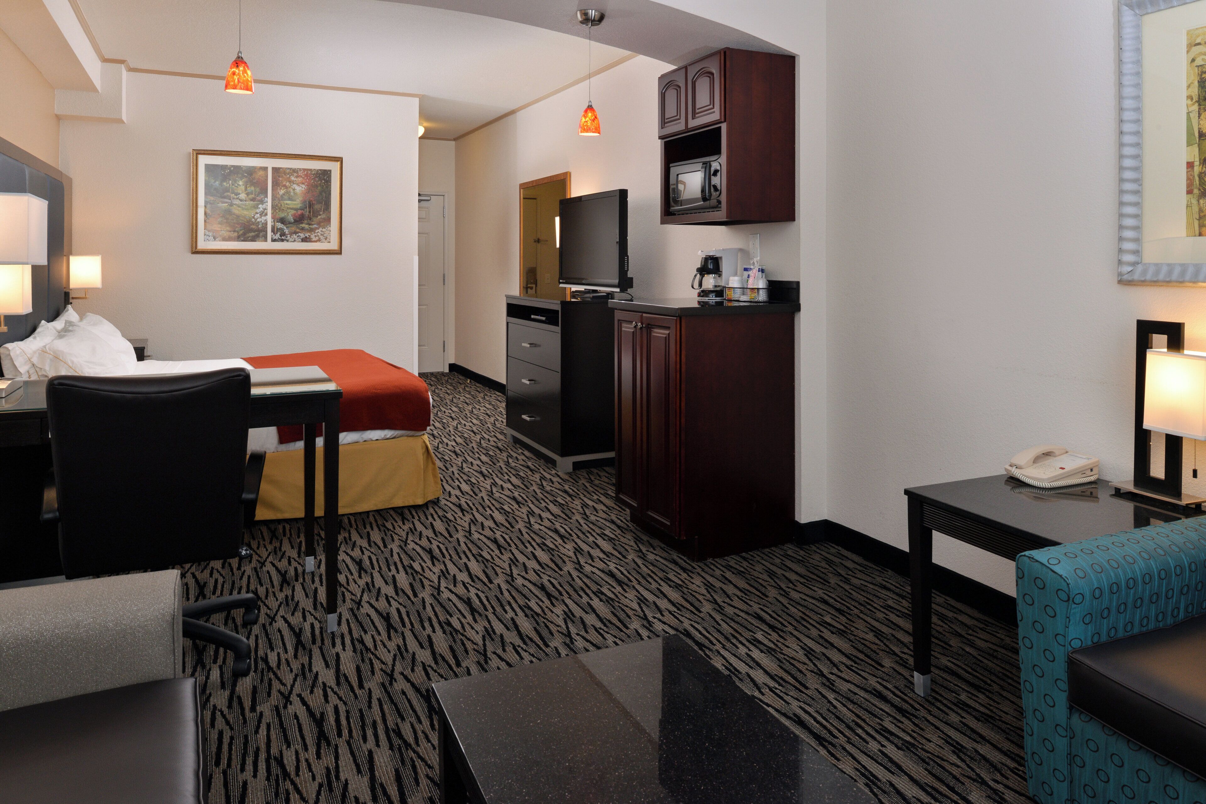 Une chambre d’hôtel équipée d’un lit, d’un bureau, d’une chaise, d’une kitchenette et d’un téléviseur.