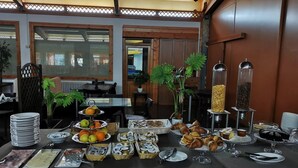Une table de buffet garnie de divers plats et couverts, entourée de murs en bois et surmontée d’un plafond avec des poutres apparentes.