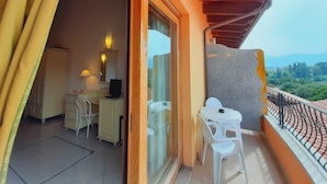 Un balcon avec une table et des chaises, un bureau avec une chaise, et une fenêtre donnant sur un paysage verdoyant et des montagnes.