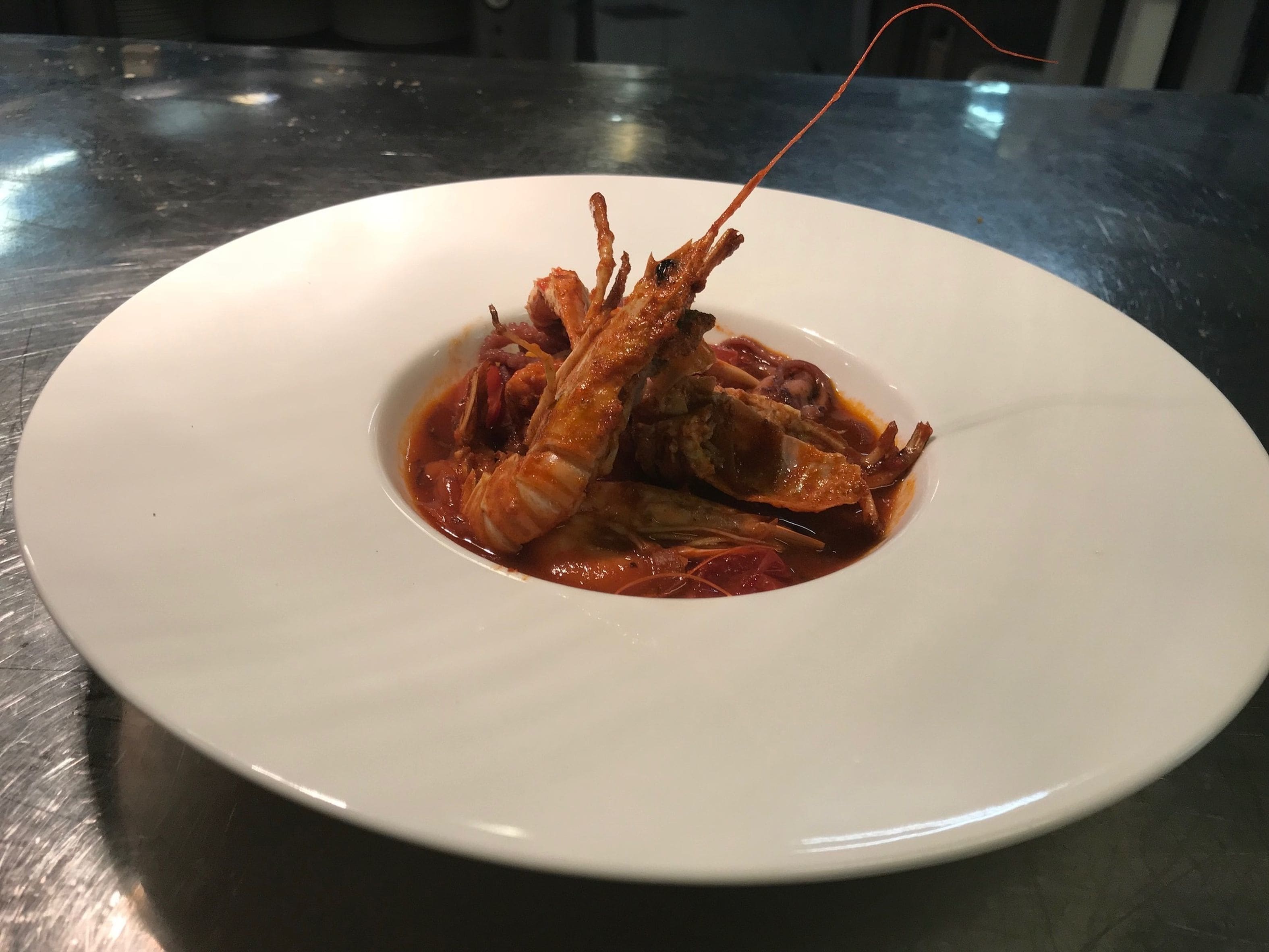 A white plate with a seafood dish, possibly lobster, on a dark countertop.
