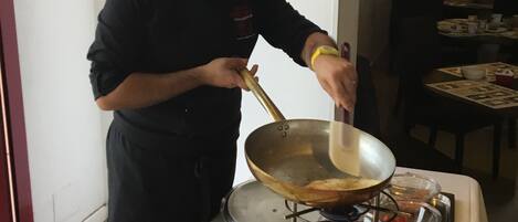 A chef cooking on a portable stove in a dining area with a table set for service.