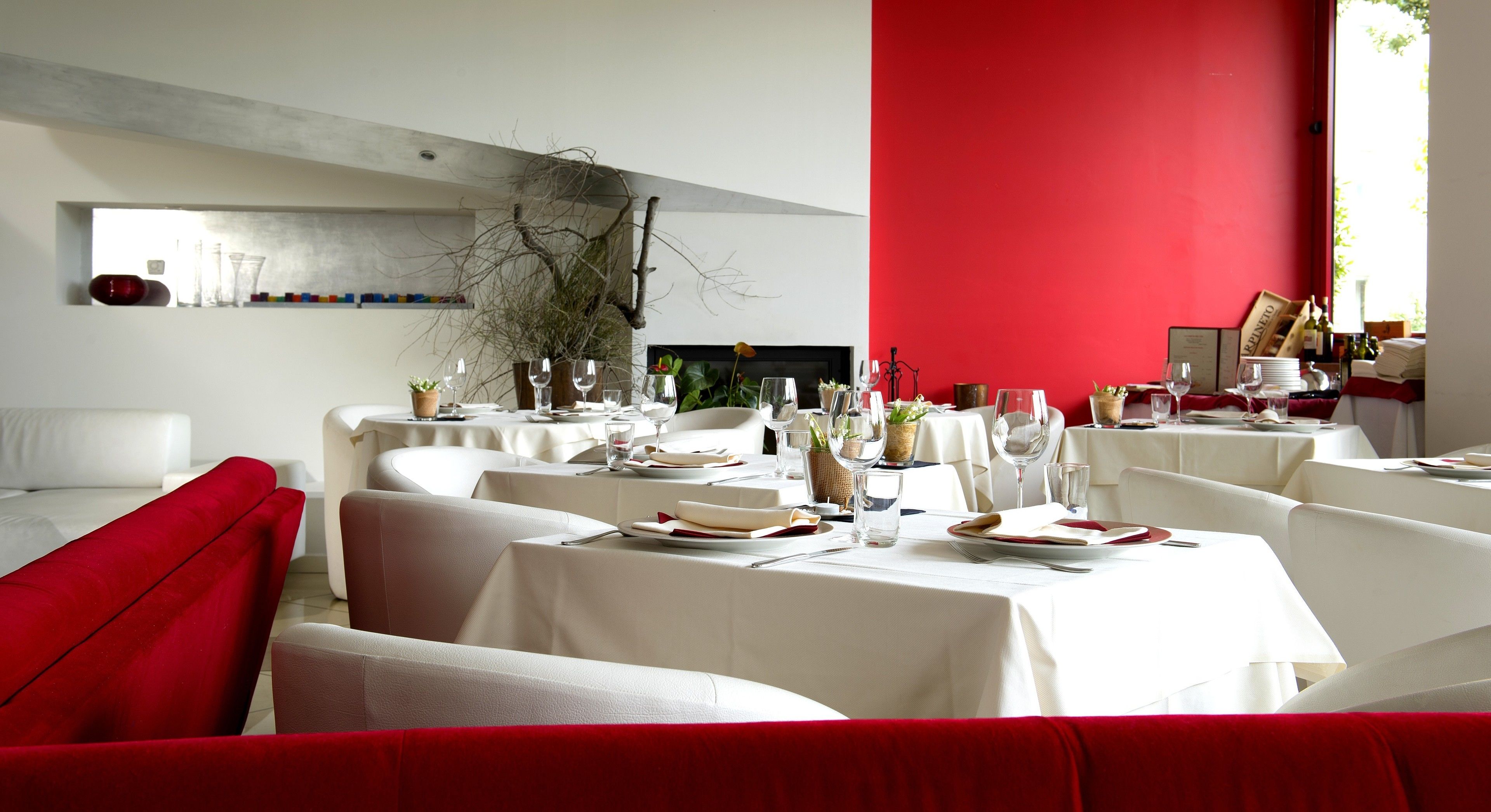 A modern dining area with white tables and red accents, featuring a minimalist design and natural decor elements.