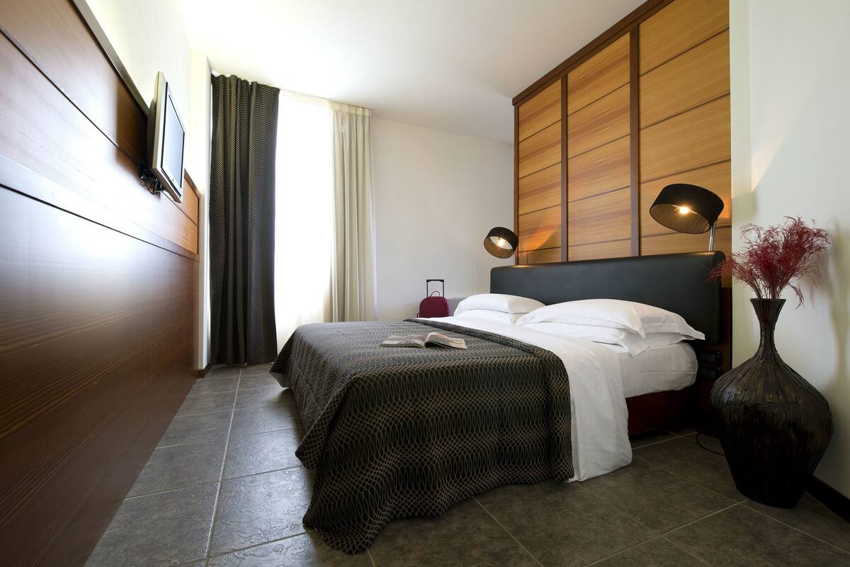 Un dormitorio moderno con una cama, una mesita de noche, una lámpara y un jarrón grande.