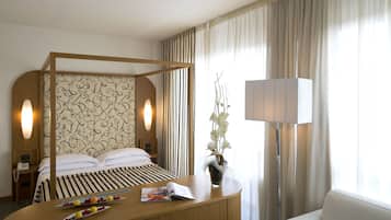 Ein Hotelzimmer mit Himmelbett, Nachttisch mit Zeitschrift und Früchten, Lampe und Blumen in einer Vase.