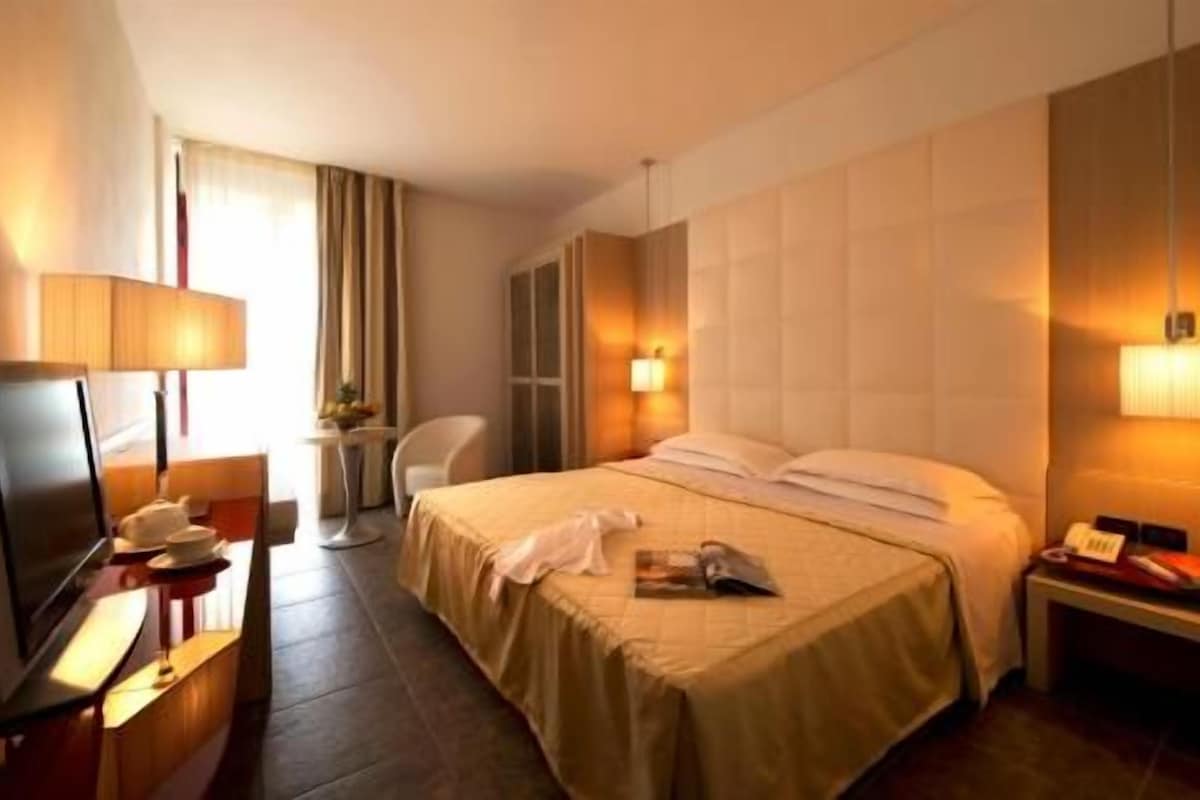 Een hotelkamer met een bed, een bureau met een lamp, een stoel en een nachtkastje met een telefoon.