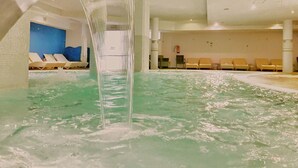 Ein Innenpool mit Wasserfall, Liegestühlen und einer Rezeption.
