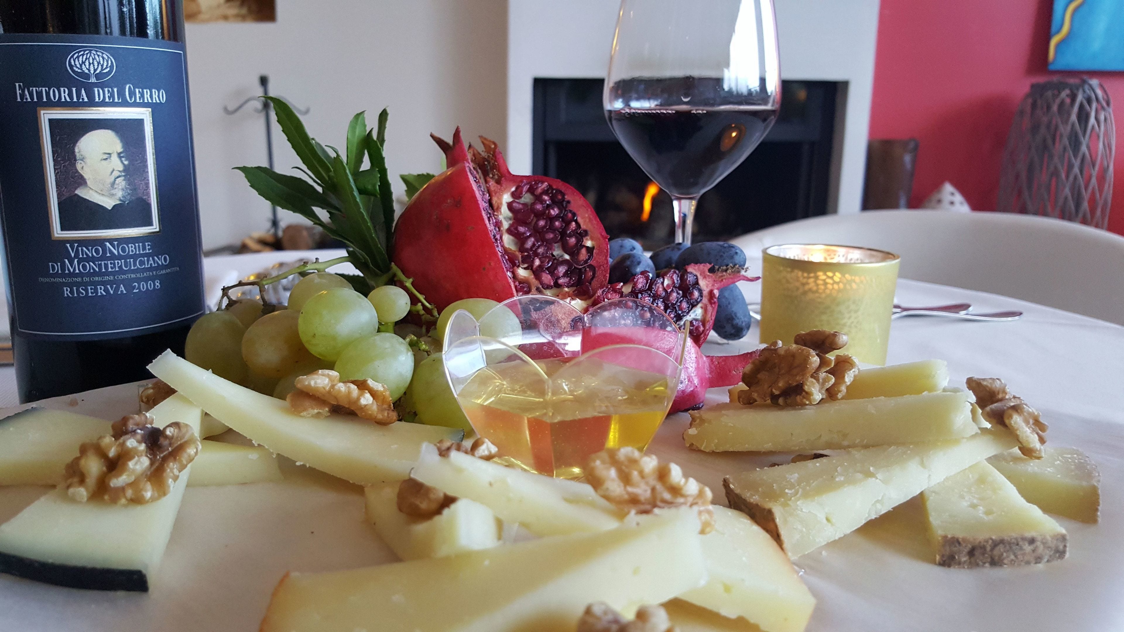 A table with a bottle of wine, a glass of wine, fruits, and cheese.