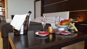 Ein Hotelzimmer mit einem Bett, einem Nachttisch mit einer Champagnerflasche, zwei Champagnergläsern, einer Obstschale und einer Kerze.