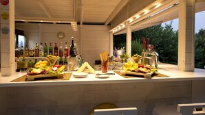 Ein Außenbereich mit Bar, der mit einer Holzbalkendecke versehen ist, mit verschiedenen Flaschen, Gläsern und einem Buffet mit Obst und Gemüse.