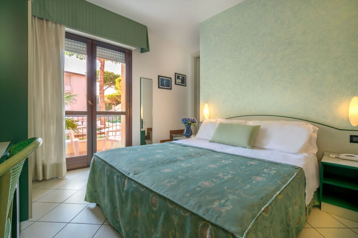 A hotel room with a bed, a nightstand, a chair, a window with curtains, and a view of the outside.