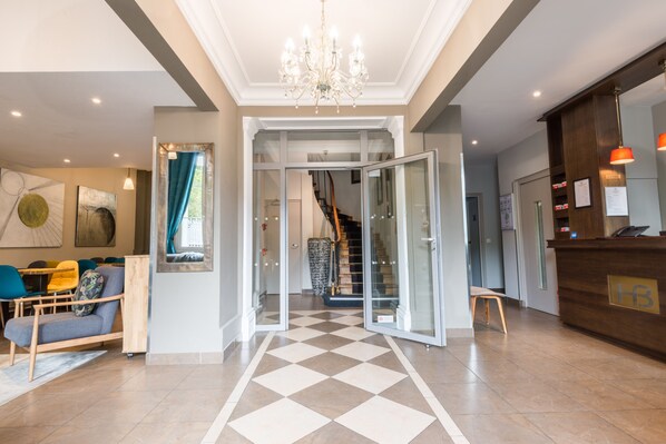 A hotel lobby with a check-in counter, a staircase, and a seating area with chairs and a sofa.