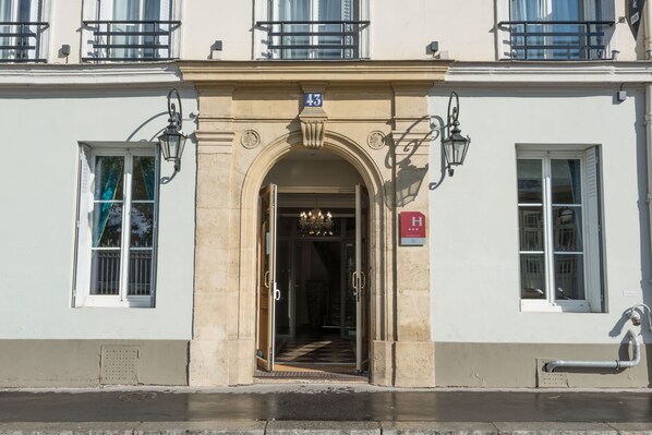 Un edificio con una amplia entrada arqueada, un letrero con el número '43' en la parte superior e indicación de hotel con una 'H'.