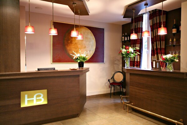 A hotel reception area with a wooden reception desk, a large abstract painting on the wall, and a bar area with bottles and glasses.