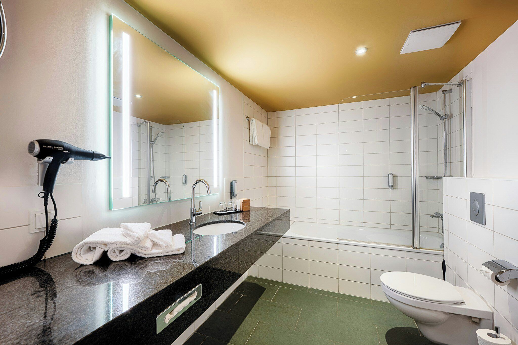 Un bany modern amb un mirall gran, un lavabo, un vàter i una zona de dutxa.