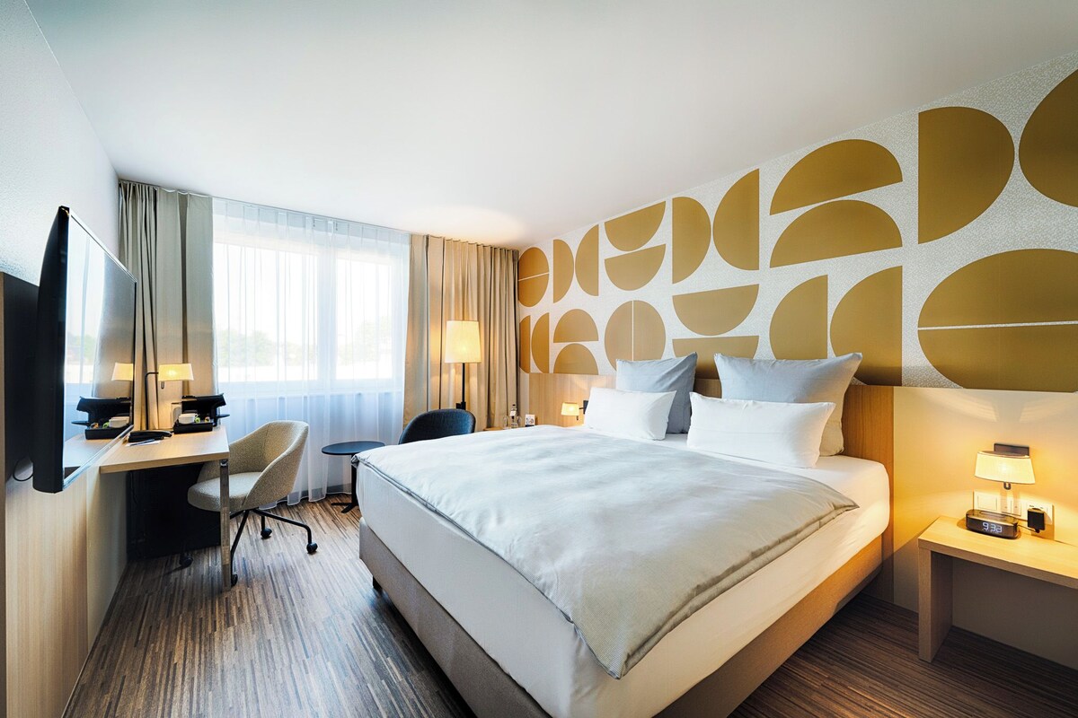 A hotel room with a large bed, a desk, a chair, and a TV.